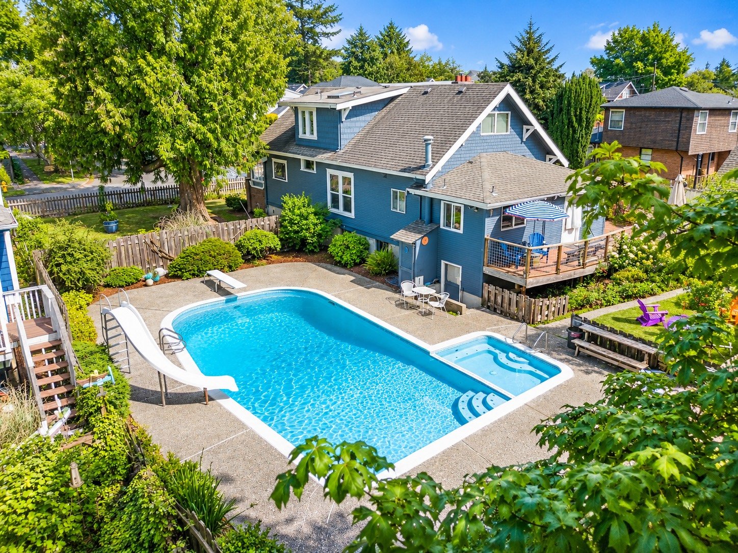 Elevated view of a blue-gray home, landscaped backyard and swimming pool with a slide.