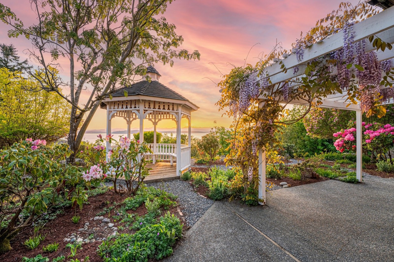 Garden with a white gazebo and flowering pergola overlooking Puget Sound at sunset.