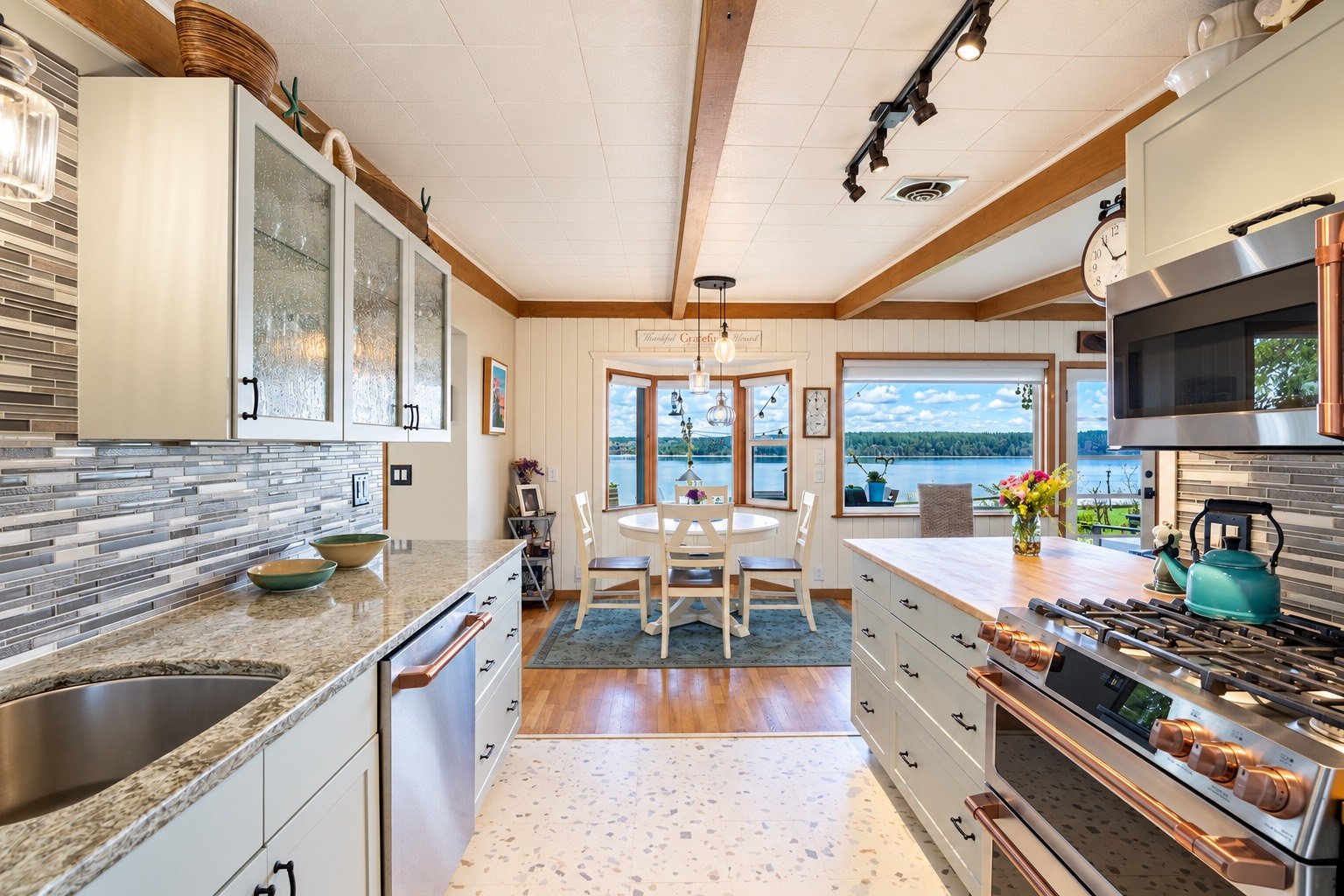 Kitchen with white cabinetry and a gas range leading to a dining area with water-view windows.