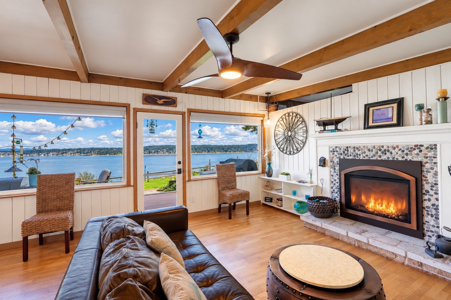 Living room with a glowing fireplace, exposed wood beams and large windows overlooking the water.